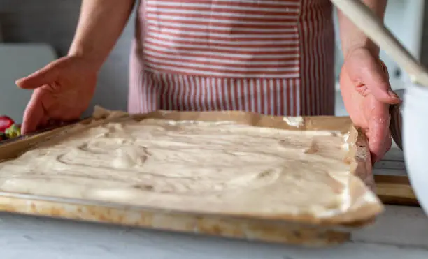 Woman is holding a baking sheet with freshly spread dough in her hands in the kitchen.
