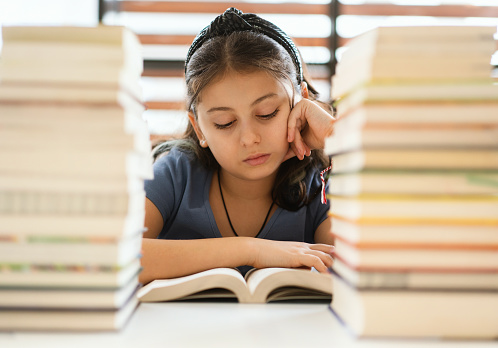 Portrait of a young girl sits on table with stack of books