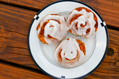 fresh-baked cinnamon rolls with icing on wooden deck