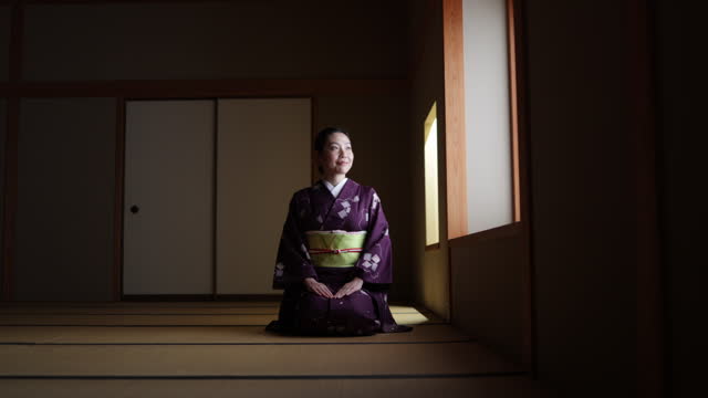 Female tourist in purple kimono sitting on heels in dark Japanese tatami room and bowing - slow motion - part 1 of 4