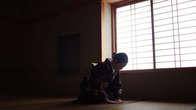 Female tourist in purple kimono sitting on heels in dark Japanese tatami room and bowing - slow motion - part 1 of 2