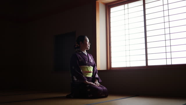 Female tourist in purple kimono sitting on heels in dark Japanese tatami room and bowing - slow motion - part 2 of 2