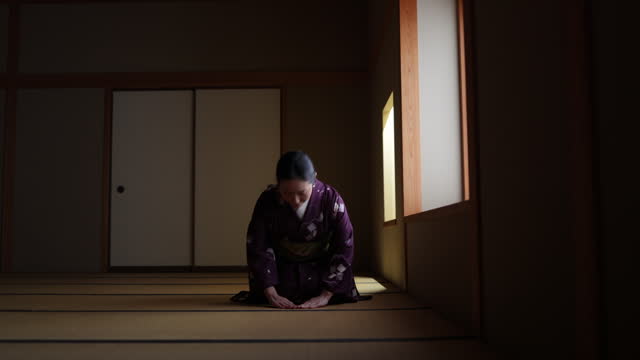 Female tourist in purple kimono sitting on heels in dark Japanese tatami room and bowing - slow motion - part 2 of 4