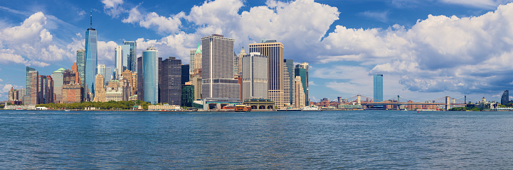 New York City Skyline with Manhattan Financial District, Battery Park, World Trade Center, Staten Island Ferry, Brooklyn Bridge, Manhattan Bridge, Blue Sky with Puffy Clouds and Water of New York Harbor. High Resolution Stitched Panoramic image with 3:1 image aspect ratio. This image was downsized to 50MP. Original image resolution is 79MP or 15,429 x 5,143 px. Canon EOS 6D Full Frame Sensor Camera and Canon EF 85mm f/1.8 USM Prime Lens.
