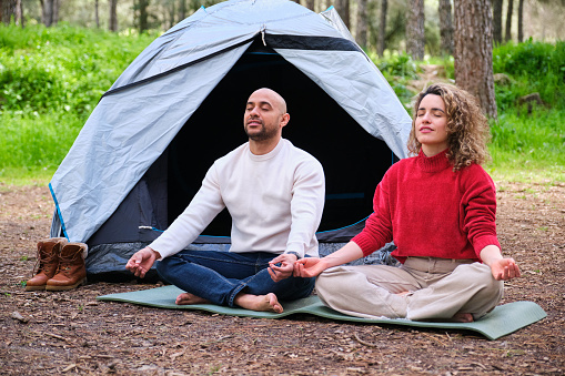 A man and woman are sitting in a tent in the woods, meditating. The scene is peaceful and serene.
