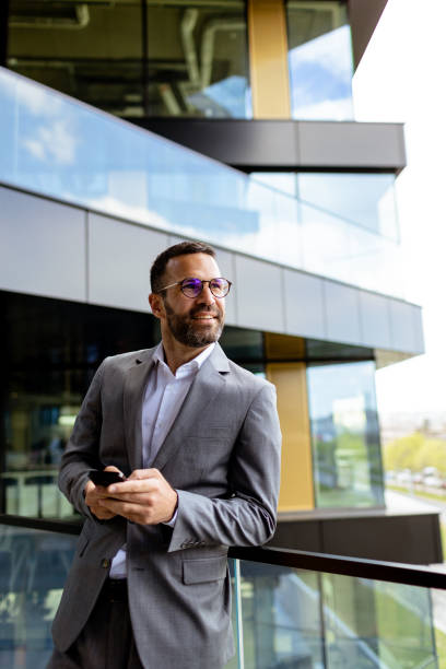 Confident Businessman Smiling in Sharp Suit Against Modern Glass Office Facade