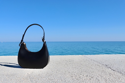 Black handbag on the beach with the sea in the background
