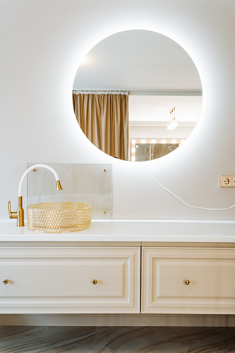 A bathroom with a white sink, tap, and round mirror. It also features wooden cabinetry and a bathroom cabinet for storage. Interior design at its finest