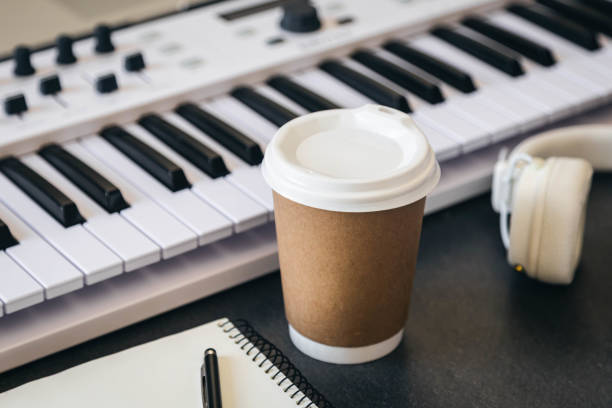 Musician workplace table with paper cup and white piano keyboard.