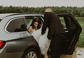 The groom helps the bride out of the car.