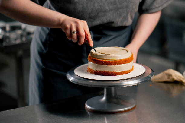 istock close up female baker in a professional kitchen distributes cream onto a sponge cake with a spatula 2148851693