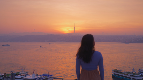 A multiracial female solo traveler is looking at the beautiful city and nature view of Istanbul from a rooftop during her travel in Türkiye Turkey.