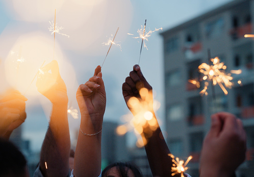 Hands, sparklers and celebration of friends in city at party outdoor in town together with fire, light or flame. Firework, glow and group of people closeup on holiday or vacation with firecracker