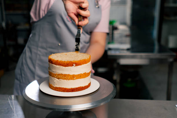 istock close up female baker in a professional kitchen distributes cream onto a sponge cake with a spatula 2148853713