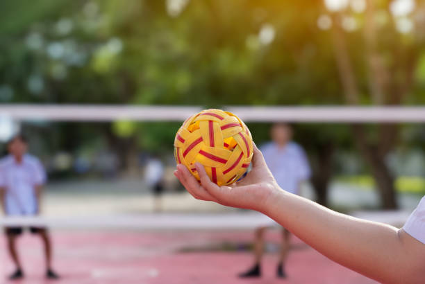 Sepak takraw ball, southeast asian countries traditional sport, holding in hand of young asian female sepak takraw player in front of the net before throwing it to another player to kick over the net.