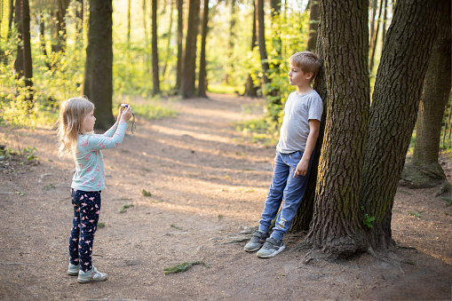 A boy teaches a little girl to take photographs in nature with a camera, child development, photography as a children's hobby Two little kids having fun together