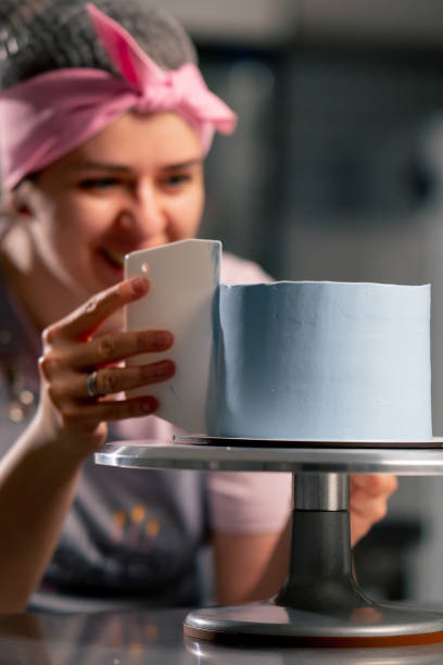 istock close up female baker in a professional kitchen distributes blue cream onto a sponge cake with a spatula 2148854394