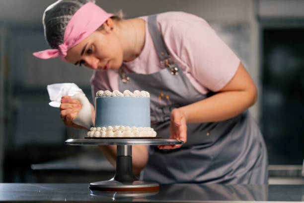 istock of a female baker in a professional kitchen decorating a blue cake with cream 2148855010