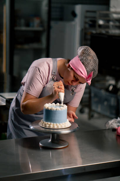 istock of a female baker in a professional kitchen decorating a blue cake with cream 2148855096