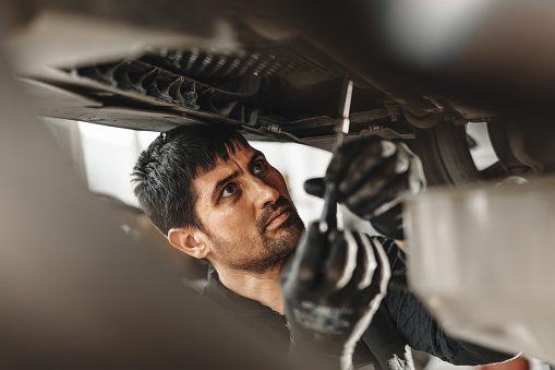 Workman mechanic working under car in auto repair shop close up