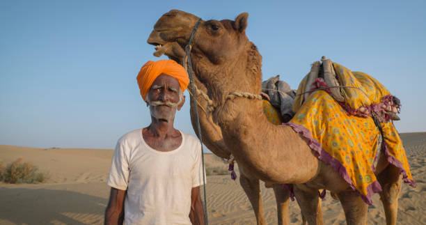 istock Indian man posing with camels on sand dunes, Rajasthan, India 2148858671