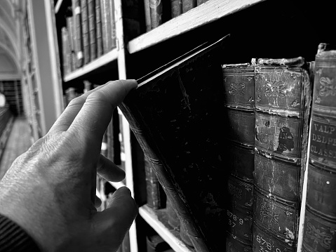 A human hand selecting a book from a bookshelf