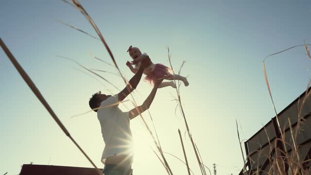 Dad throws a small child up into the sky and catches it in the rays of the rising sun in the backlight, a romantic video of a happy family and spending time