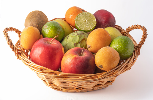 Wicker basket full of fresh and assorted fruit on a white background