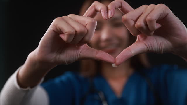 A closeup portrait of an excited smiling young woman makes her hands in the heart shape of fingers saying I love you to the audience.
