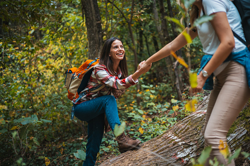 Happy women help while hiking up a rocky mountain in nature with backpack. Females friends exercise in nature park climbing and jumping while with sportswear training or trekking together outdoors
