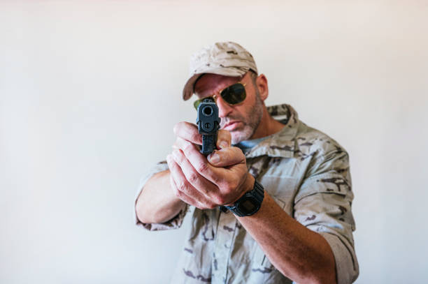 Handsome man wearing camouflage military uniform and aiming with gun.