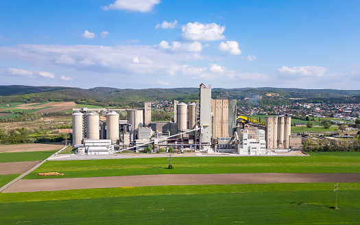 Mannersdorf, Austria - April 30, 2023: Huge cement factory surrounded by agricultural fields and beautiful natural landscape