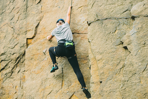 Young athletic woman in equipment doing rock climbing outdoors. Training area for outdoor activities. Extreme sport.