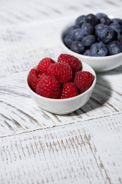 This is an overhead photo of a heart bowl of berries on a white wood background