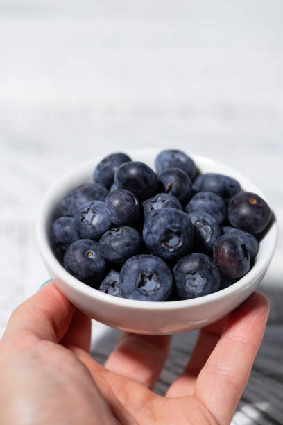istock fresh blueberries in a white bowl in hand, vertical 2148866013