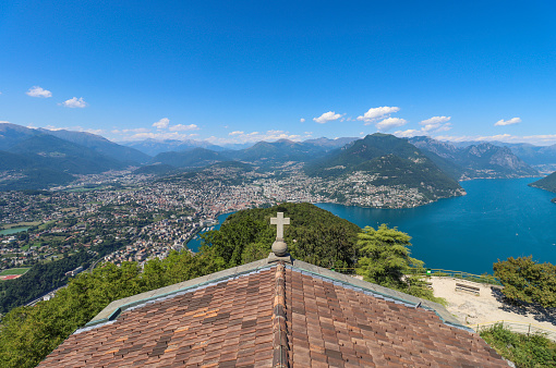 People standing at a viewpoint on San Salvatore mountain overlooking Lake Lugano.