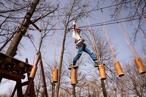 A boy in a helmet climbs a rope park in the spring
