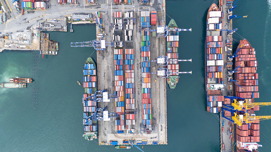Aerial top view of container ship in port at container terminal port, aerial view of container ship standing in terminal port and loading, unloading container with cranes. Commercial cargo container  ship in sea port.