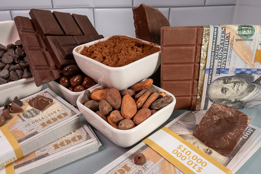 Concept of rising prices of chocolate. Chocolate bars, powder, beans, chips with stacks of 100 dollar bills and currency. High quality photo