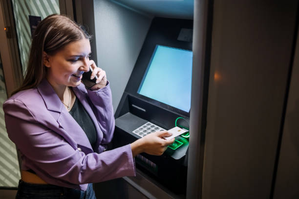 istock Single person in front of ATM at night inserting credit card while having a call on mobile phone 2148869905