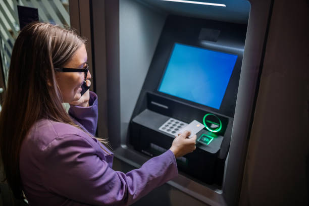 istock Single person in front of ATM at night inserting card while having a call on mobile phone 2148869943