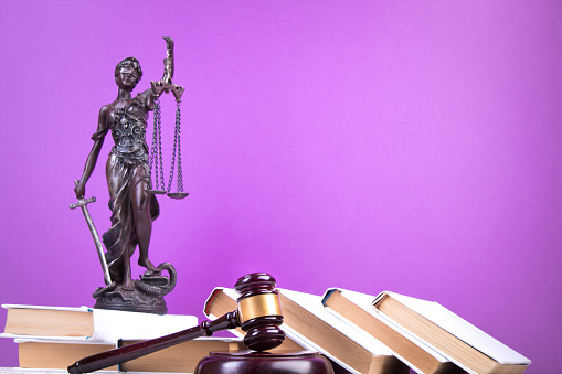 Law concept - Open law book, Judge's gavel, scales, Themis statue on table in a courtroom or law enforcement office. Wooden table, purple background