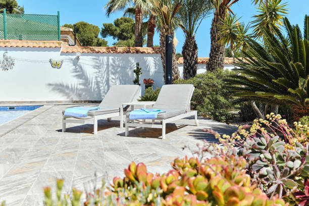 istock Two deck-chairs in poolside on tropical bushes and palm trees background 2148871272