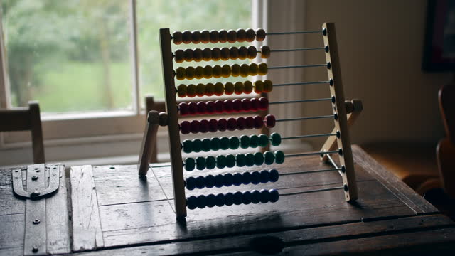 Multicolored abacus standing on a weathered wood table, with a backdrop of natural light and greenery. Ideal for educational, historical, and arithmetic visual concepts