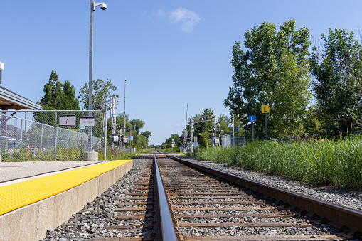 Empty railroad tracks with yellow safety line - surrounded by greenery - clear blue sky. Taken in Toronto, Canada.