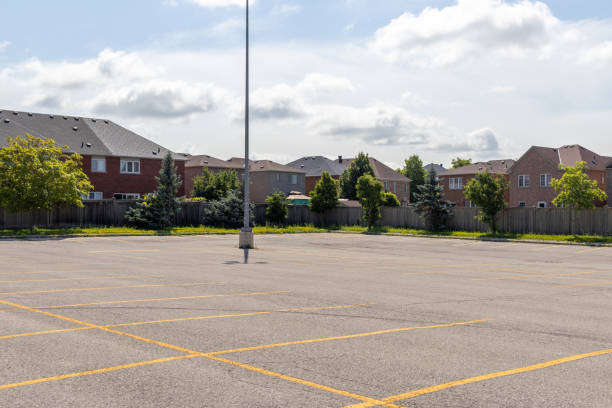 istock Empty parking lot with lined spaces - lone light pole - suburban homes background - clear sky with clouds 2148874795
