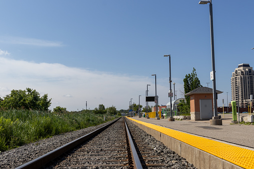 Empty railroad tracks with yellow safety line - surrounded by greenery - clear blue sky. Taken in Toronto, Canada.