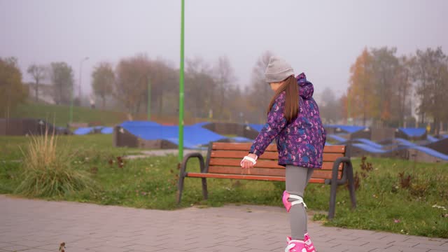 Little girl in knee and elbow defense learning to skating roller skates outdoors at foggy day