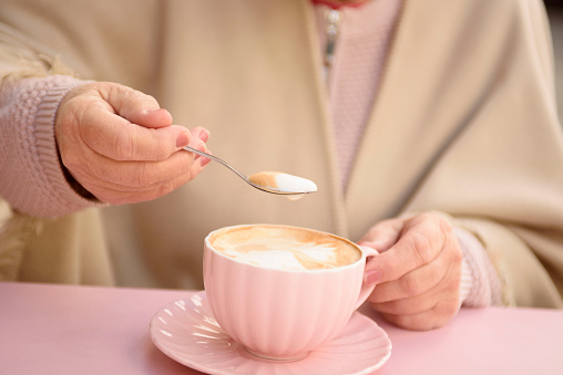 A woman in a cafe drinks cappuccino in a pink cup. Coffee time.