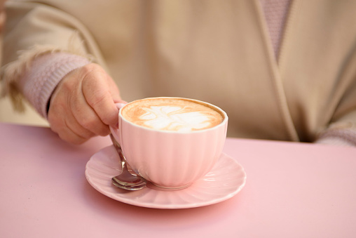 A woman in a cafe drinks cappuccino in a pink cup. Coffee time.